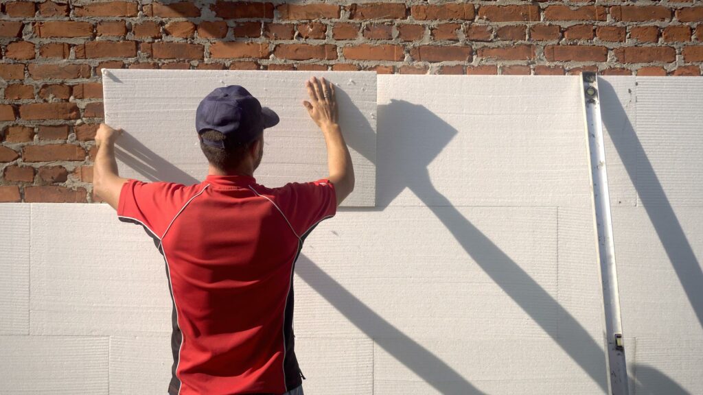 Ein Handwerker bringt ein Wärmedämmverbundsystem WDVS an der Fassade eines Hauses an.